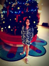 Full length portrait of happy girl standing at illuminated christmas tree