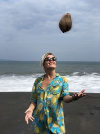 Young woman wearing sunglasses standing at beach against sky