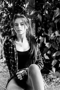 Portrait of young woman sitting against trees