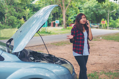 Woman talking on phone while standing by broken down car