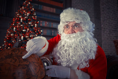 Man wearing santa claus costume pointing at globe at home