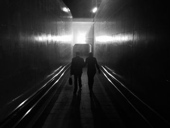 Rear view of people walking in illuminated tunnel