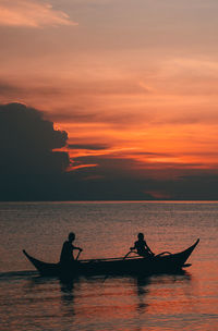 Silhouette people in sea against sky during sunset