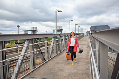 Portrait of smiling mid adult woman walking with suitcase on footbridge