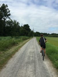 Rear view of man riding bicycle on dirt road