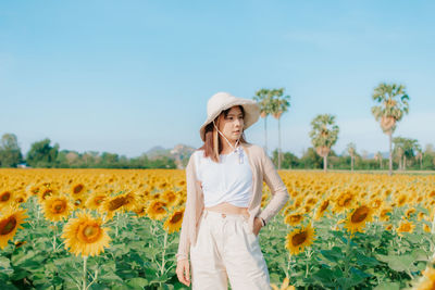 Woman standing on sunflower field against clear sky