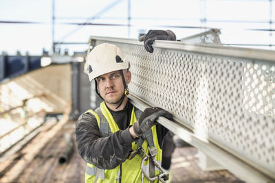 Construction worker looking away while carrying metal plank at site