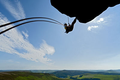 Low angle view of man hanging on rope against sky