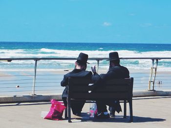 Rear view of man sitting on bench at beach