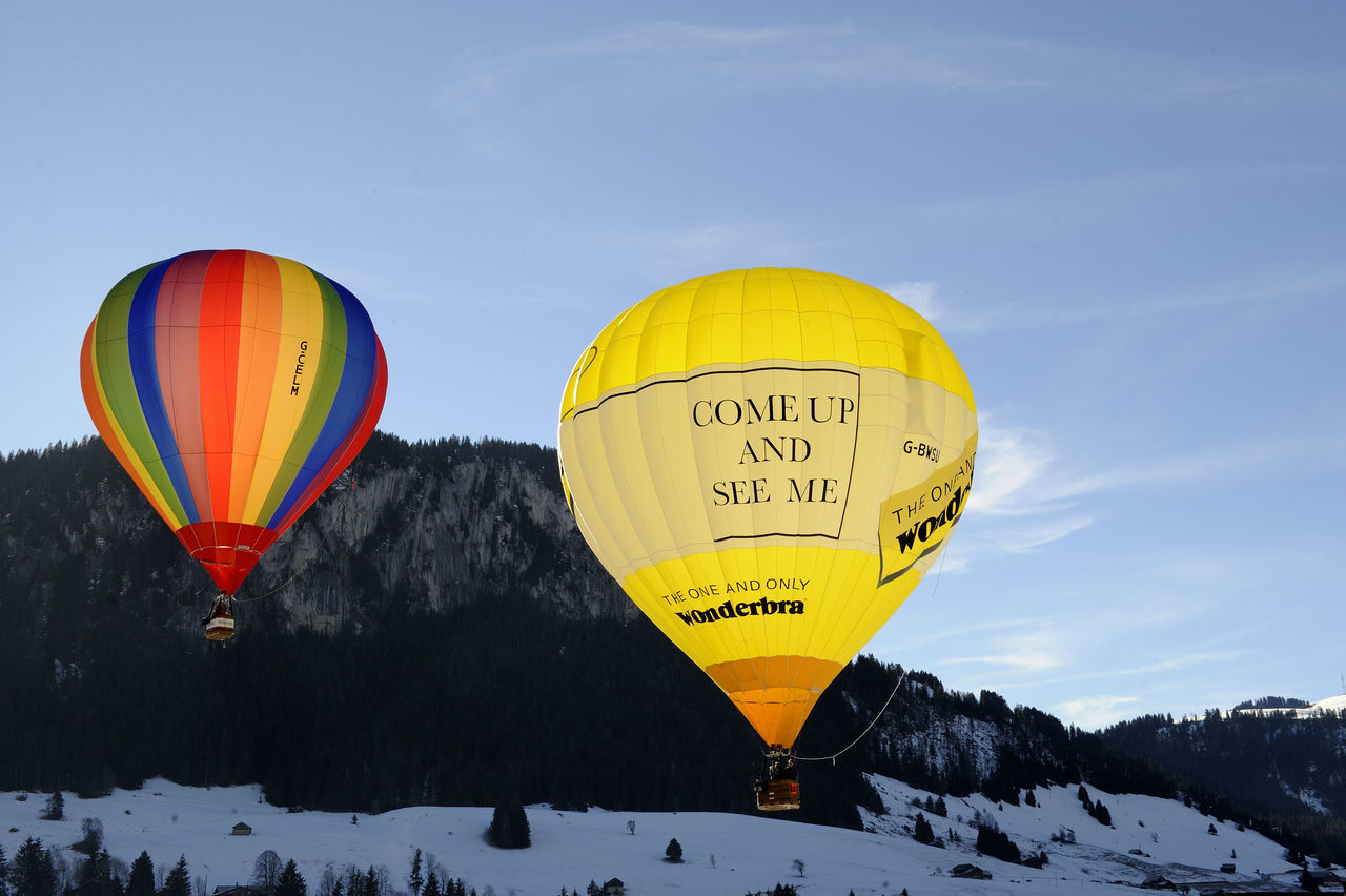 HOT AIR BALLOON FLYING OVER MOUNTAIN AGAINST SKY DURING WINTER