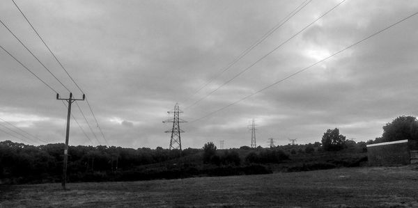 Electricity pylon on field against cloudy sky