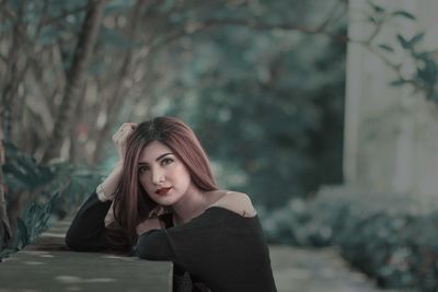 Portrait of young woman leaning by plants