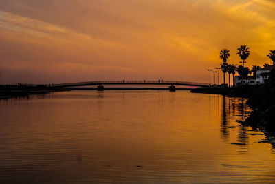 Silhouette bridge over river against orange sky