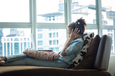 Side view of woman sitting on sofa at home