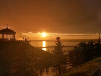 Silhouette trees by sea against sky during sunset