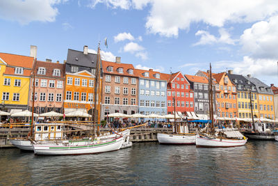 Sailboats moored on canal by buildings in city against sky