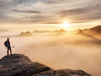 Tired hiker with sporty backpack on rocky peak and watching into deep misty valley bellow. sunny day