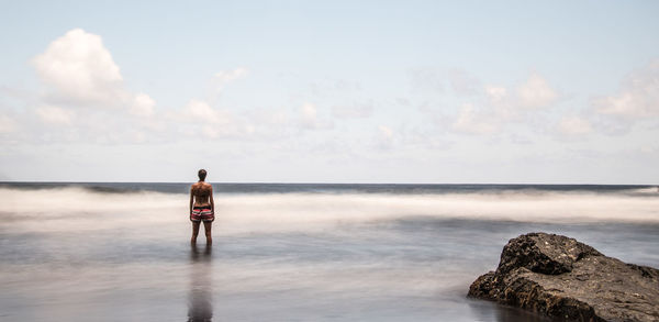 Rear view of woman standing at beach against sky