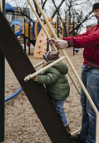 Father assisting son in climbing slide at playground