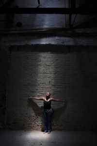 Mature woman with arms outstretched standing against wall