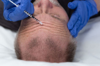 Cropped hands of doctor injecting on man face