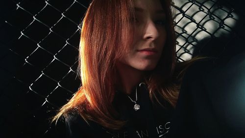 Portrait of beautiful young woman seen through chainlink fence
