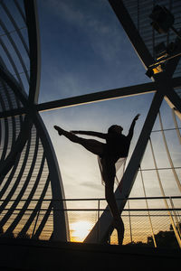 Low angle view of silhouette man standing on metallic structure against sky