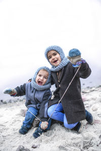 Portrait of cute cheerful sibling sitting by lake during winter