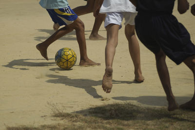 Low section of boys playing soccer at beach