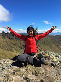 Young latin woman sitting doing yoga on a mountain top with blue sky on background