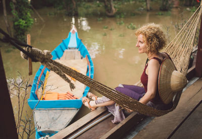 Side view of mid adult woman looking away while sitting on hammock over lake