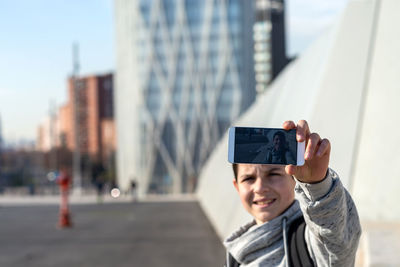Outdoor portrait of young teen with mobile phone taking a selfie