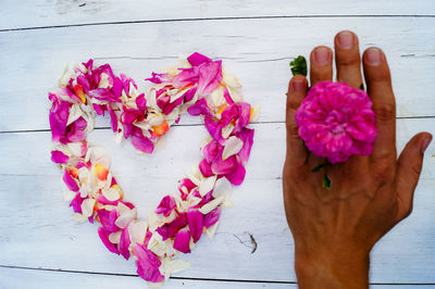 High angle view of heart shape made with petals by man hand holding flower on table