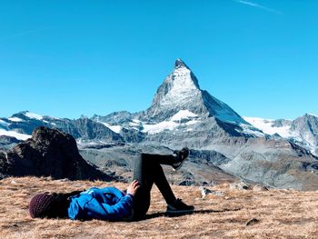 Side view of woman lying on mountain against clear blue sky