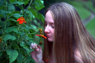 Close-up of woman smelling red flower blooming on plant