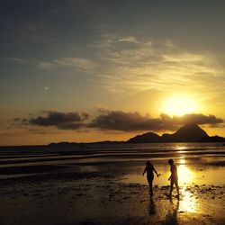 Silhouette people standing on beach against sky during sunset