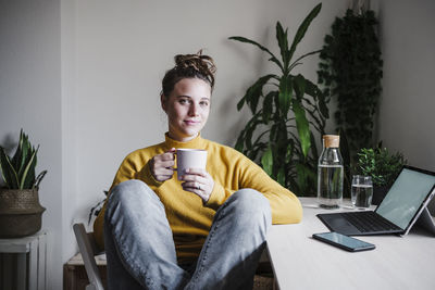 Smiling woman drinking coffee while sitting at home office