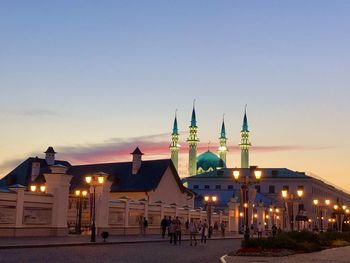 People in illuminated building against sky during sunset in city