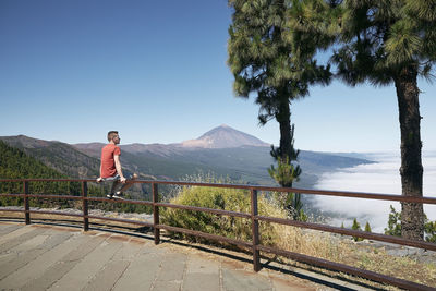 Man sitting on railing and looking to beautiful landscape above clouds against pico de teide. 