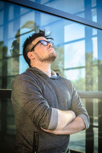 Young man looking away while standing against window