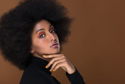 Portrait of beautiful woman with afro hairstyle against brown background