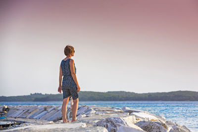 Rear view of man standing by sea against clear sky