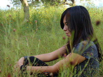 Young woman looking away sitting amidst plants on field