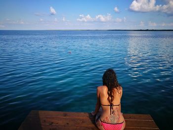Rear view of woman wearing bikini sitting against sea on jetty