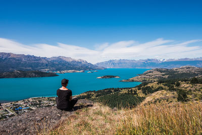 Rear view of woman sitting on mountain against sky