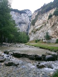 Scenic view of waterfall by cliff against sky