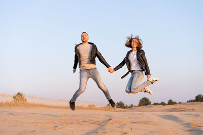 Young couple jumping against clear sky at desert