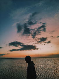 Rear view of man looking at sea against sky during sunset