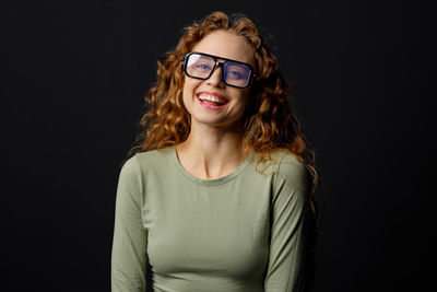 Portrait of young woman wearing sunglasses against black background