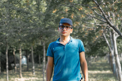 Mature man wearing cap and eyeglasses standing against trees in forest